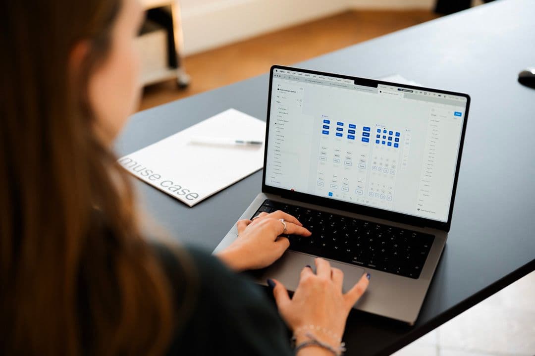 Lächelnde Frau arbeitet an einem muse case MacBook in einem modernen Büro.