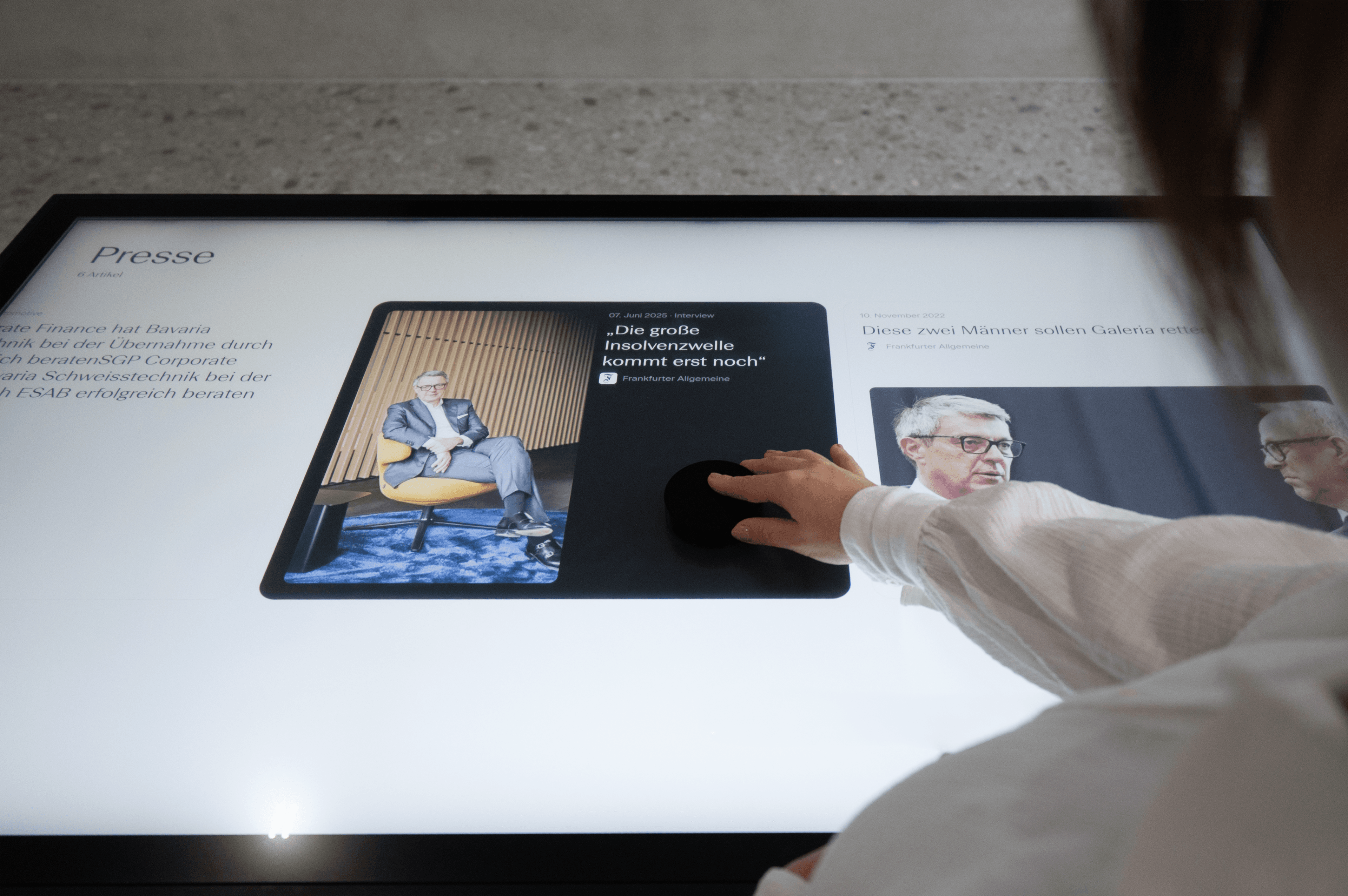 Die Hand einer Person interagiert mit einem großen Touchscreen, auf dem Nachrichtenartikel angezeigt werden.